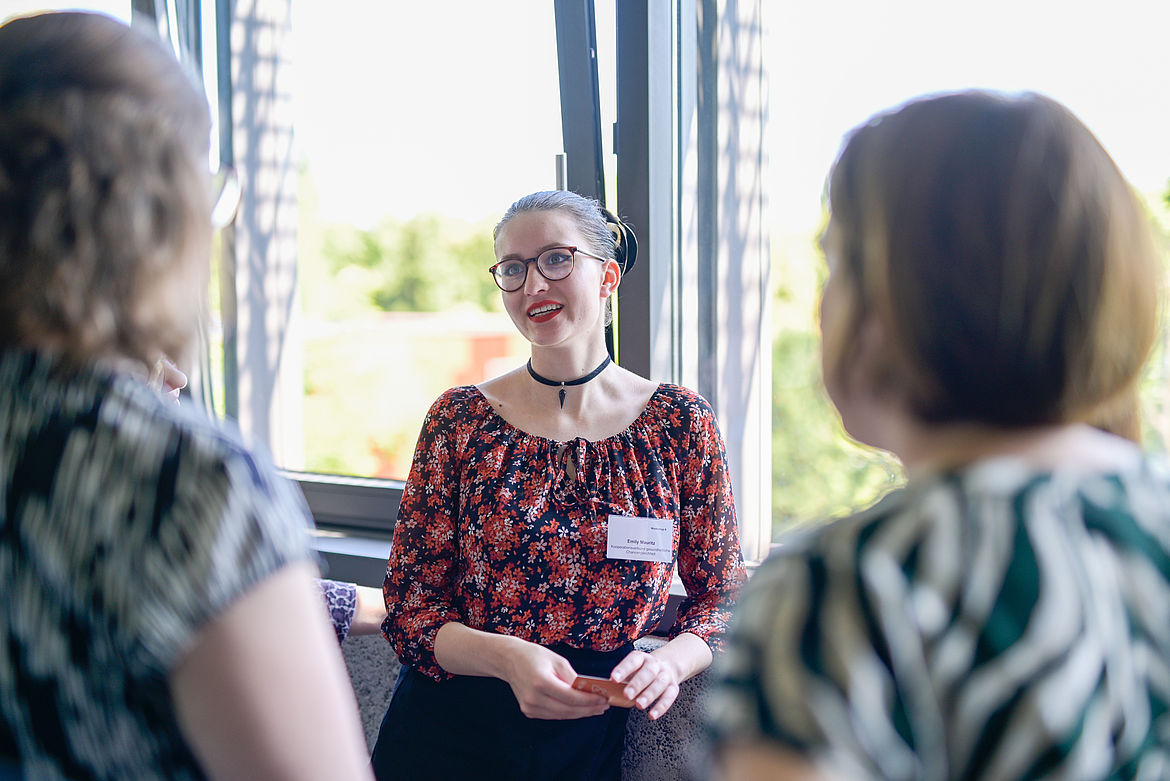Impression aus Workshop 6 „Ressourcenstärkende Ansätze“ Eine Teilnehmende steht am Fenster und spricht mit anderen Teilnehmenden ihrer Kleingruppe.