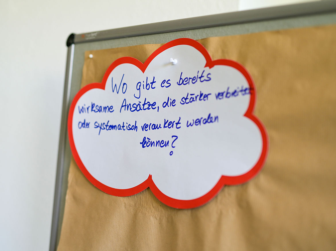 Impression aus Workshop 1 „Länderperspektive – Psyche und Gesundheit“ Auf einer Moderationstafel ist eine Karte in Form einer Wolke gepinnt. Auf der Karte steht die Frage „Wo gibt es bereits wirksame Angebote, die stärker verbreitet oder systematisch verankert werden können?“